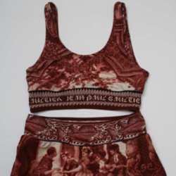 The two-piece consists of a cropped top and skirted bikini bottoms and is printed in sepia tones with images of architecture.  It has the words ‘Gaultier ete 1998' printed in a cartouche on the back of the bikini bottoms and the words ‘Jean Paul Gaultier' printed on a band at the base of the cropped top. 